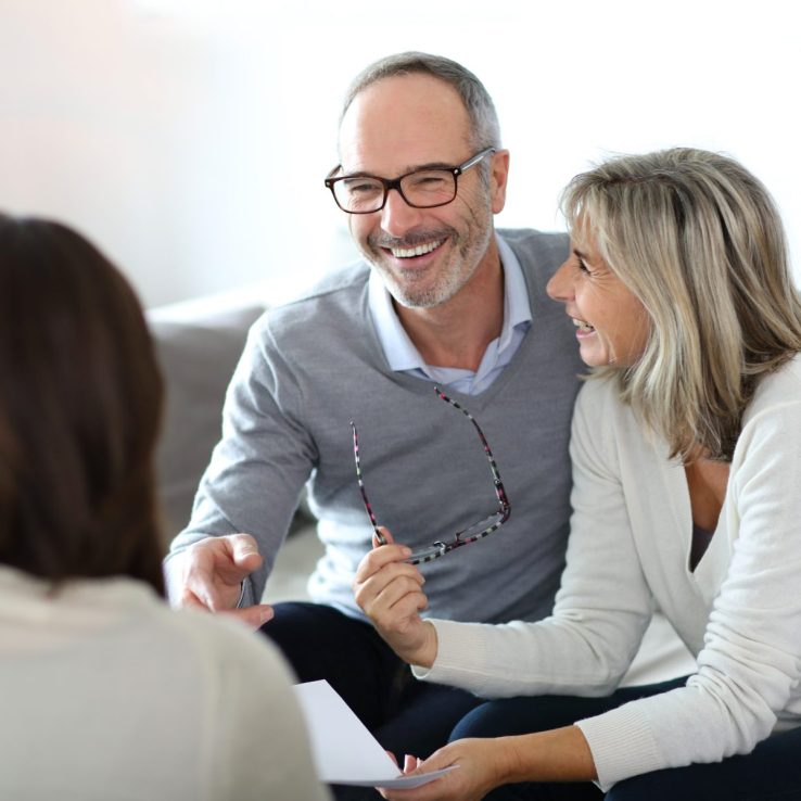 A smiling couple sitting on a couch while engaging in conversation with a consultant.