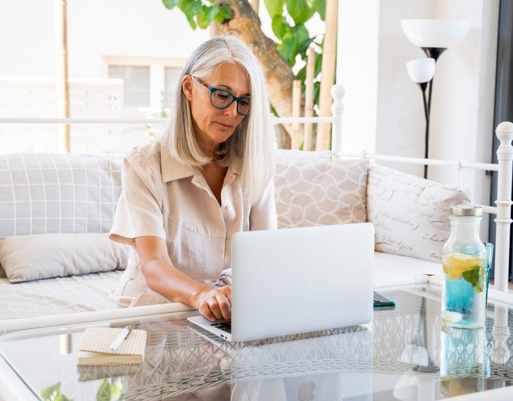 mature entrepreneur woman working from home with laptop in porch during daytime