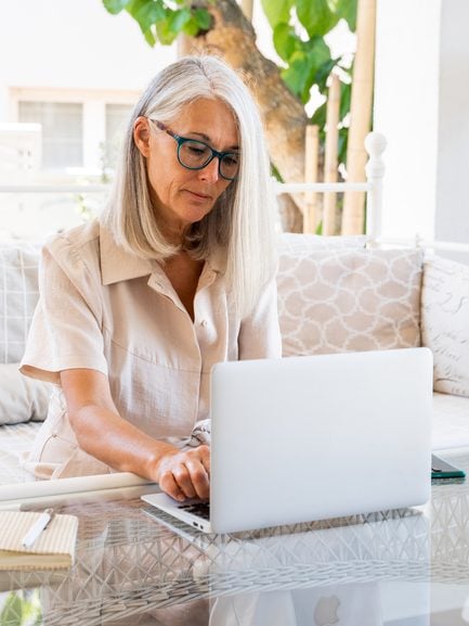 mature entrepreneur woman working from home with laptop in porch during daytime